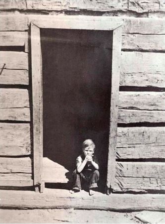 TAT picture 13B - A boy sitting in the doorway of a log cabin.